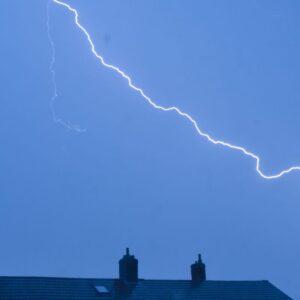 a lightning flashing on a dark blue sky over two chimneys